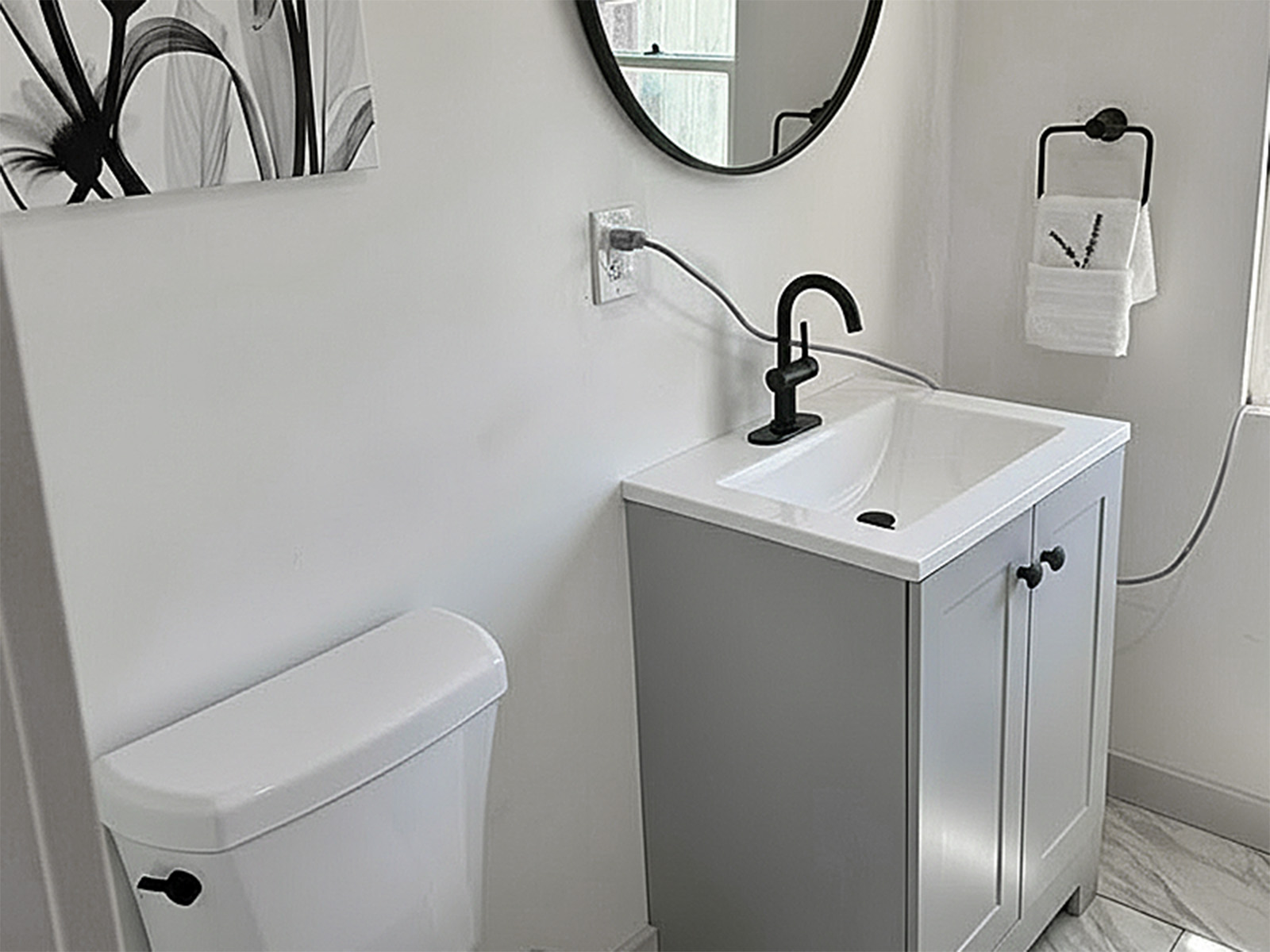Full bathroom remodel including compact vanity installation with plumbing hookup, toilet replacement, contemporary matte black faucet and hardware, decorative mirror mounting, towel bar installation, and professional tile flooring